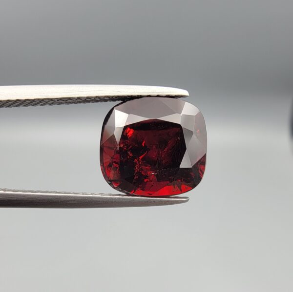 ​A 6.81-carat natural red garnet from Madagascar, featuring a deep reddish color and sparkling faceted cut, professionally displayed in a white jeweler's box.