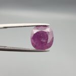 A large 6.83-carat natural Madagascar ruby with a purplish-red color, featuring visible natural mountain marks and cracks on the surface and back, displayed in a jeweler's box.