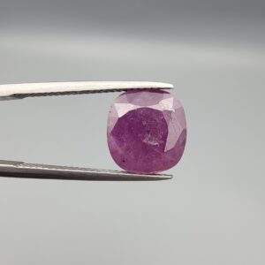 A large 6.83-carat natural Madagascar ruby with a purplish-red color, featuring visible natural mountain marks and cracks on the surface and back, displayed in a jeweler's box.