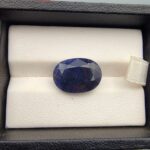 A massive 11.25-carat natural blue sapphire from Afghanistan with an oval faceted cut and deep blue color, professionally displayed in a white jeweler's box.