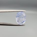 A rare 2.17-carat unheated natural blue sapphire (Neelam) from Ceylon, Sri Lanka, featuring a masterfully faceted oval cut and natural light blue silk-like bands, held in professional jeweler's tweezers.