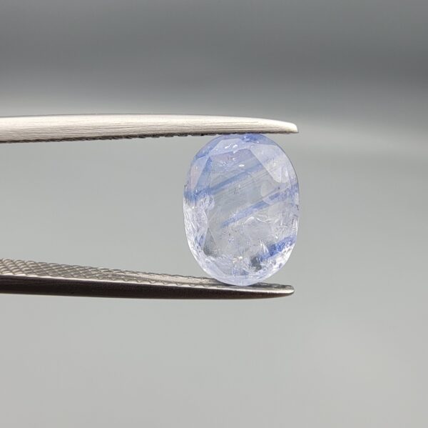 A rare 2.17-carat unheated natural blue sapphire (Neelam) from Ceylon, Sri Lanka, featuring a masterfully faceted oval cut and natural light blue silk-like bands, held in professional jeweler's tweezers.