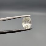 A rare 1.25-carat unheated natural white sapphire (Safed Neelam) from Ceylon, Sri Lanka, featuring a masterfully faceted oval cut and exceptional colorless clarity, presented in professional jeweler's tweezers.