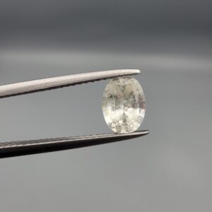 A rare 1.25-carat unheated natural white sapphire (Safed Neelam) from Ceylon, Sri Lanka, featuring a masterfully faceted oval cut and exceptional colorless clarity, presented in professional jeweler's tweezers.