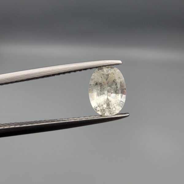 A rare 1.25-carat unheated natural white sapphire (Safed Neelam) from Ceylon, Sri Lanka, featuring a masterfully faceted oval cut and exceptional colorless clarity, presented in professional jeweler's tweezers.