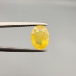 A rare 1.50-carat unheated natural yellow sapphire (Pukhraj) from Ceylon, Sri Lanka, featuring a masterfully faceted oval cut and bright lemon-yellow saturation, presented in a professional white jeweler's box.