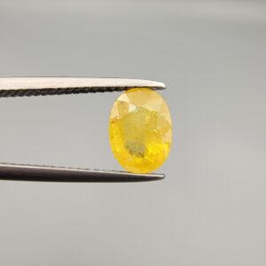 A rare 1.50-carat unheated natural yellow sapphire (Pukhraj) from Ceylon, Sri Lanka, featuring a masterfully faceted oval cut and bright lemon-yellow saturation, presented in a professional white jeweler's box.