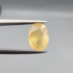 A rare 1.97-carat unheated natural yellow sapphire (Pukhraj) from Ceylon, Sri Lanka, featuring a masterfully faceted oval cut and deep golden-yellow saturation, presented in professional jeweler's tweezers.