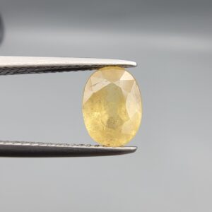 A rare 1.97-carat unheated natural yellow sapphire (Pukhraj) from Ceylon, Sri Lanka, featuring a masterfully faceted oval cut and deep golden-yellow saturation, presented in professional jeweler's tweezers.