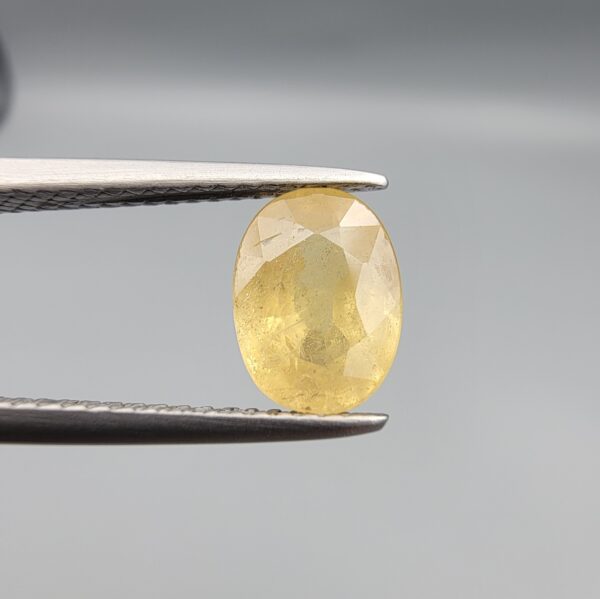 A rare 1.97-carat unheated natural yellow sapphire (Pukhraj) from Ceylon, Sri Lanka, featuring a masterfully faceted oval cut and deep golden-yellow saturation, presented in professional jeweler's tweezers.
