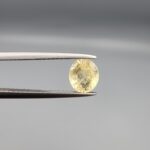 A rare 1.23-carat unheated natural yellow sapphire (Pukhraj) from Ceylon, Sri Lanka, featuring a masterfully faceted oval cut and bright lemon-yellow saturation, held in professional jeweler's tweezers.