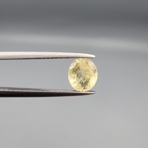 A rare 1.23-carat unheated natural yellow sapphire (Pukhraj) from Ceylon, Sri Lanka, featuring a masterfully faceted oval cut and bright lemon-yellow saturation, held in professional jeweler's tweezers.