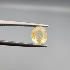 A rare 1.27-carat unheated natural yellow sapphire (Pukhraj) from Ceylon, Sri Lanka, featuring a masterfully faceted oval cut and bright lemon-yellow saturation, held in professional jeweler's tweezers.