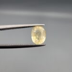 A rare 1.59-carat unheated natural yellow sapphire (Pukhraj) from Ceylon, Sri Lanka, featuring a masterfully faceted oval cut and bright lemon-yellow saturation, shown in professional jeweler's tweezers.