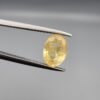 A rare 1.67-carat unheated natural yellow sapphire (Pukhraj) from Ceylon, Sri Lanka, featuring a masterfully faceted oval cut and bright lemon-yellow saturation, shown in professional jeweler's tweezers.