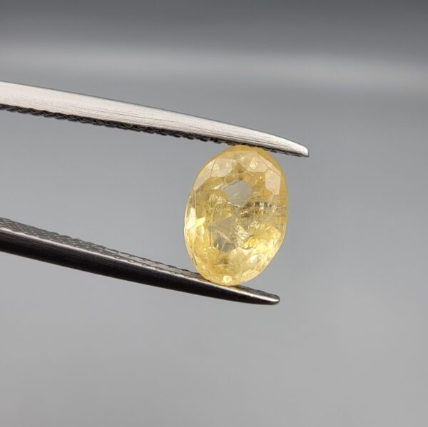 A rare 1.67-carat unheated natural yellow sapphire (Pukhraj) from Ceylon, Sri Lanka, featuring a masterfully faceted oval cut and bright lemon-yellow saturation, shown in professional jeweler's tweezers.