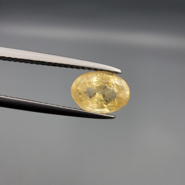 A rare 1.67-carat unheated natural yellow sapphire (Pukhraj) from Ceylon, Sri Lanka, featuring a masterfully faceted oval cut and bright lemon-yellow saturation, shown in professional jeweler's tweezers.