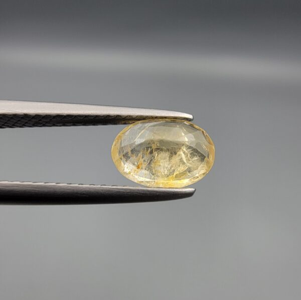 A rare 1.67-carat unheated natural yellow sapphire (Pukhraj) from Ceylon, Sri Lanka, featuring a masterfully faceted oval cut and bright lemon-yellow saturation, shown in professional jeweler's tweezers.