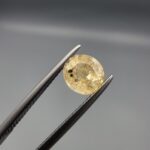 A rare 1.43-carat unheated natural yellow sapphire (Pukhraj) from Ceylon, Sri Lanka, featuring a masterfully faceted oval cut and bright lemon-yellow saturation, shown in professional jeweler's tweezers.