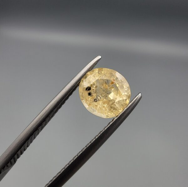 A rare 1.43-carat unheated natural yellow sapphire (Pukhraj) from Ceylon, Sri Lanka, featuring a masterfully faceted oval cut and bright lemon-yellow saturation, shown in professional jeweler's tweezers.