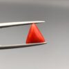 A 2.20-carat natural Italian red coral in a polished triangle cabochon shape, showcasing a smooth surface and rich orange-red tone in a jeweler's display.
