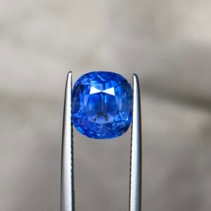 ​A 5.27 carat natural blue sapphire (Neelam) featuring a cushion and mixed cut with transparent to semi-transparent clarity, as shown in its GGI laboratory certificate.