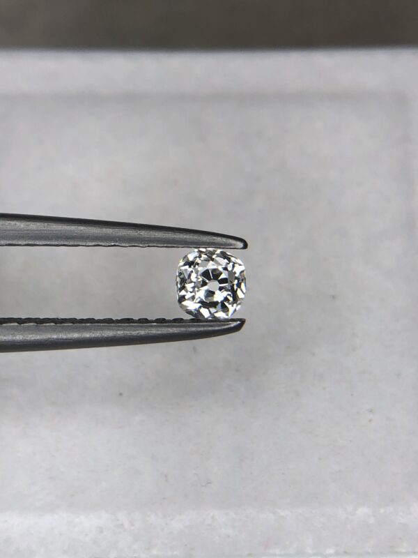 A 0.23-carat natural white diamond (Heera) with a brilliant cushion shape cut, displaying high fire and sparkle under professional lighting, held in jeweler's tweezers.