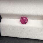 A 1.22-carat natural red ruby from Mozambique with a round brilliant cut, showcasing vibrant red color and high clarity, professionally displayed in a white jeweler's box.