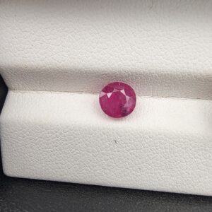 A 1.22-carat natural red ruby from Mozambique with a round brilliant cut, showcasing vibrant red color and high clarity, professionally displayed in a white jeweler's box.