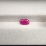 A 1.10-carat natural pinkish-red ruby from Mozambique with an oval faceted cut, displaying high clarity and brilliant luster, presented in a white jeweler's box.