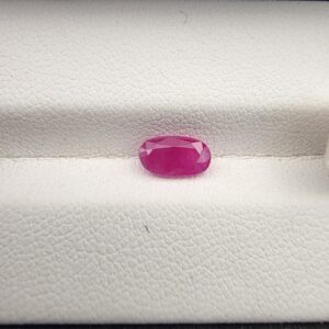 A 1.10-carat natural pinkish-red ruby from Mozambique with an oval faceted cut, displaying high clarity and brilliant luster, presented in a white jeweler's box.