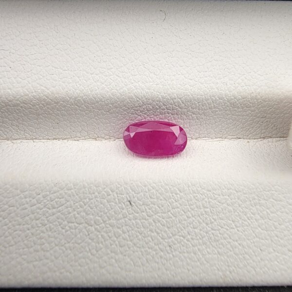 A 1.10-carat natural pinkish-red ruby from Mozambique with an oval faceted cut, displaying high clarity and brilliant luster, presented in a white jeweler's box.