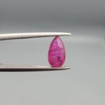 A 1.14-carat natural red ruby from Mozambique in a pear faceted cut, showing authentic natural surface pits and rich red color, displayed in a professional jeweler's box.
