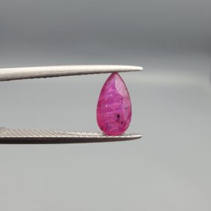 A 1.14-carat natural red ruby from Mozambique in a pear faceted cut, showing authentic natural surface pits and rich red color, displayed in a professional jeweler's box.