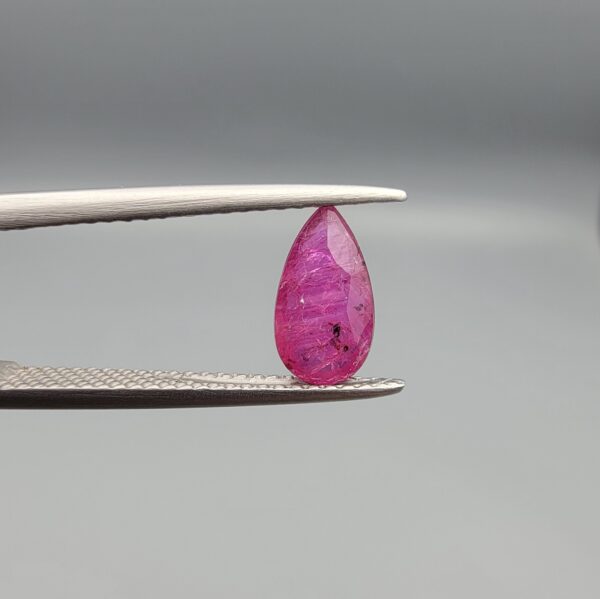A 1.14-carat natural red ruby from Mozambique in a pear faceted cut, showing authentic natural surface pits and rich red color, displayed in a professional jeweler's box.