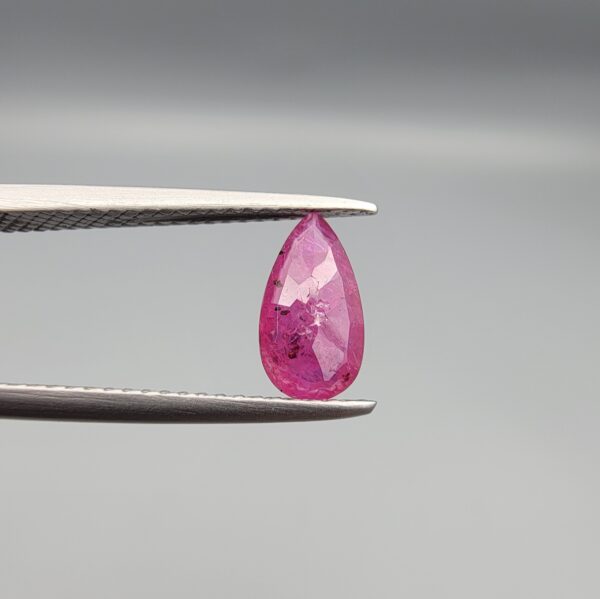 A 1.14-carat natural red ruby from Mozambique in a pear faceted cut, showing authentic natural surface pits and rich red color, displayed in a professional jeweler's box.
