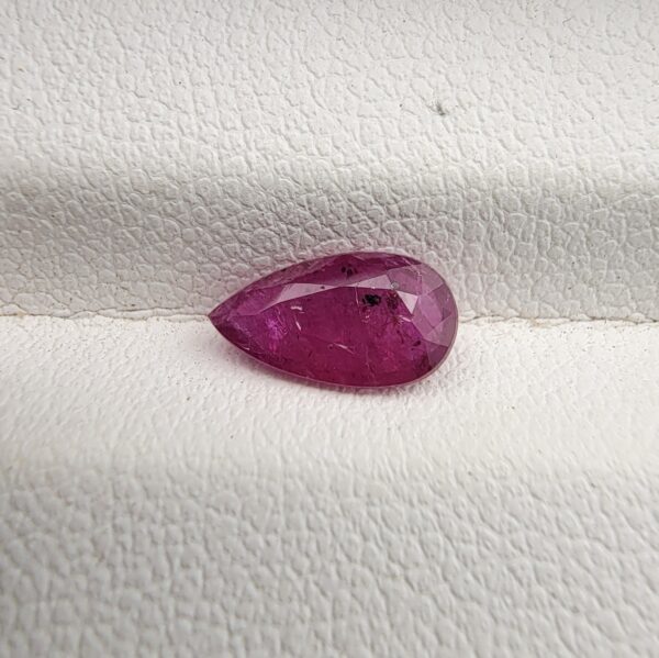 A 1.14-carat natural red ruby from Mozambique in a pear faceted cut, showing authentic natural surface pits and rich red color, displayed in a professional jeweler's box.