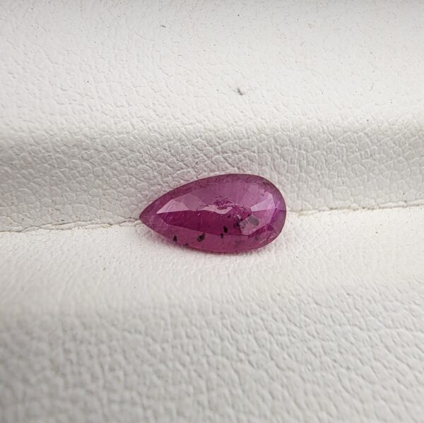 A 1.14-carat natural red ruby from Mozambique in a pear faceted cut, showing authentic natural surface pits and rich red color, displayed in a professional jeweler's box.