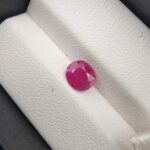 A 1.22-carat natural pinkish-red ruby from Mozambique with an oval faceted cut, showcasing excellent clarity and a vibrant "raspberry" red color, presented in a white jeweler's box.