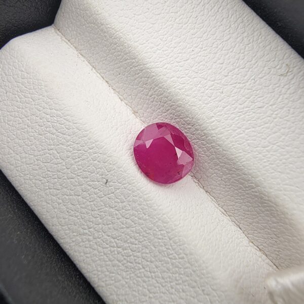 A 1.22-carat natural pinkish-red ruby from Mozambique with an oval faceted cut, showcasing excellent clarity and a vibrant "raspberry" red color, presented in a white jeweler's box.