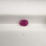A 0.74-carat natural red ruby from Mozambique with an oval faceted cut, showcasing brilliant luster and deep red saturation, displayed in a white jeweler's box.
