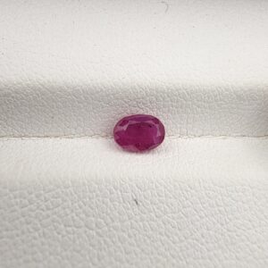 A 0.74-carat natural red ruby from Mozambique with an oval faceted cut, showcasing brilliant luster and deep red saturation, displayed in a white jeweler's box.
