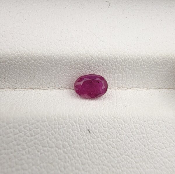 A 0.74-carat natural red ruby from Mozambique with an oval faceted cut, showcasing brilliant luster and deep red saturation, displayed in a white jeweler's box.