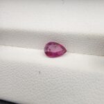 A 0.81-carat natural red ruby from Mozambique in a pear faceted cut, showing vibrant red color and an authentic natural surface pit, displayed in a professional jeweler's box.