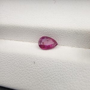 A 0.81-carat natural red ruby from Mozambique in a pear faceted cut, showing vibrant red color and an authentic natural surface pit, displayed in a professional jeweler's box.