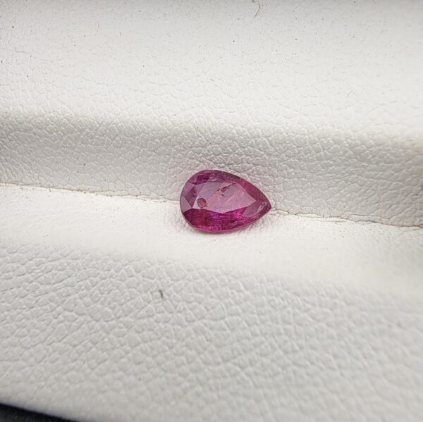A 0.81-carat natural red ruby from Mozambique in a pear faceted cut, showing vibrant red color and an authentic natural surface pit, displayed in a professional jeweler's box.