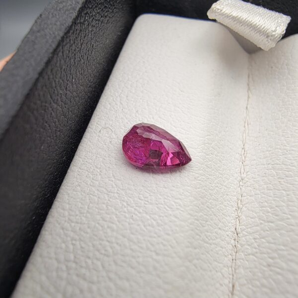 A 0.81-carat natural red ruby from Mozambique in a pear faceted cut, showing vibrant red color and an authentic natural surface pit, displayed in a professional jeweler's box.
