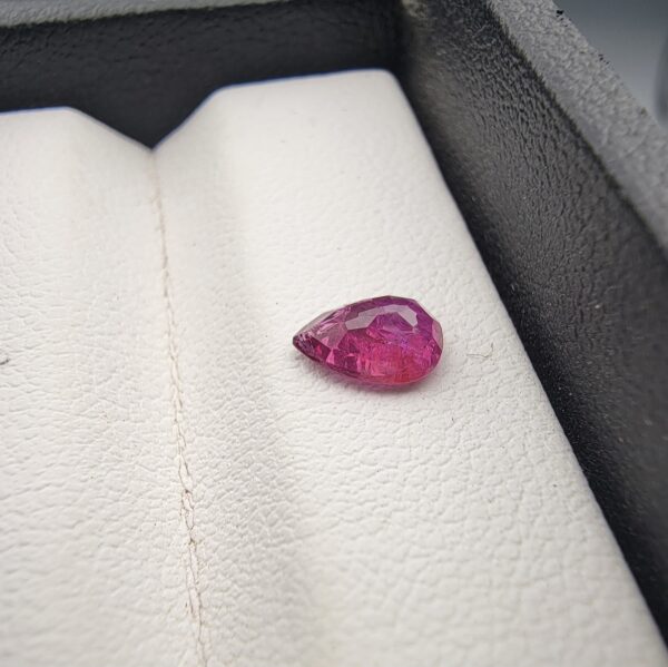 A 0.81-carat natural red ruby from Mozambique in a pear faceted cut, showing vibrant red color and an authentic natural surface pit, displayed in a professional jeweler's box.