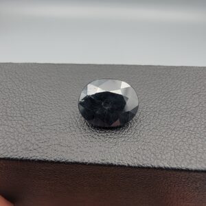 A 4.77-carat natural blue sapphire from Kanchanaburi, Thailand, featuring a classic oval faceted cut and a deep midnight blue color, displayed in a professional jeweler's box.
