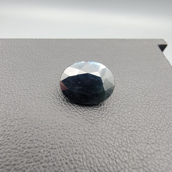 A 4.90-carat natural blue sapphire from Kanchanaburi, Thailand, featuring a classic oval faceted cut and a deep midnight blue color, displayed in a professional jeweler's box.